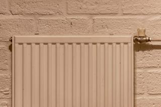 Radiateur à panneaux beige fixé sur un mur de briques peintes, robinet de réglage en laiton