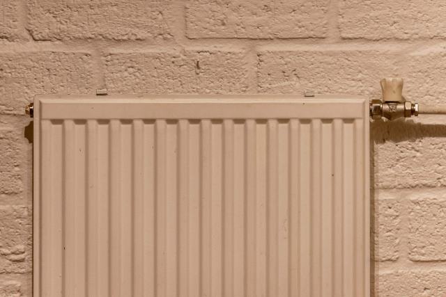 Chaudière basse température, standard ou à condensation : les différences Radiateur à panneaux beige fixé sur un mur de briques peintes, robinet de réglage en laiton