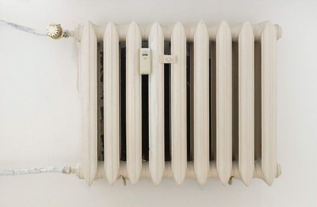 Répartiteurs de frais de chauffage sur radiateur : mesure, relève et limites Radiateur en fonte blanc équipé d'un répartiteur de frais de chauffage fixé entre ses éléments