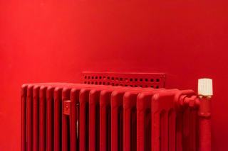 Radiateur en fonte rouge avec tête de robinet thermostatique blanche devant un mur rouge