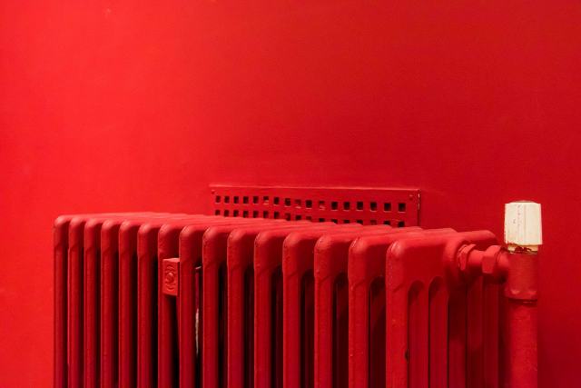 Têtes thermostatiques sur radiateur : régler chaque pièce en immeuble Radiateur en fonte rouge avec tête de robinet thermostatique blanche devant un mur rouge