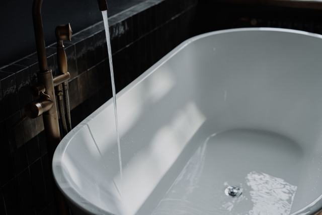 Ballon d'eau chaude couplé à la chaudière : capacité, confort et pertes Baignoire îlot blanche qui se remplit sous un robinet mural, dans une salle de bains sombre