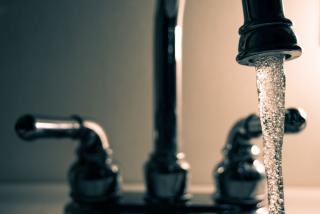 Eau qui coule d'un robinet noir à deux poignées, en gros plan