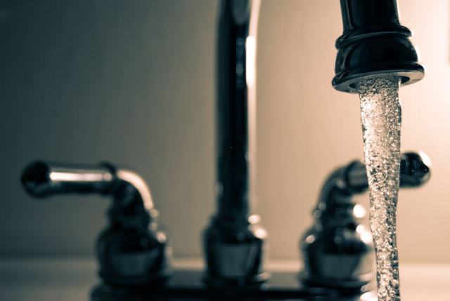 Chaudière mixte : chauffage et eau chaude par un seul appareil Eau qui coule d'un robinet noir à deux poignées, en gros plan
