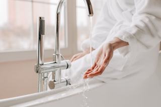 Main qui teste la température de l'eau sous le bec d'un mitigeur de baignoire chromé