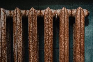 Vieux radiateur en fonte couvert de rouille contre un mur sombre