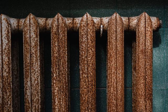 Usure d'une chaudière : réparer ou remplacer au bon moment Vieux radiateur en fonte couvert de rouille contre un mur sombre