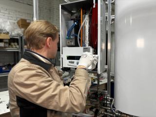 Technicien en gants blancs qui intervient sur une chaudière murale ouverte dans un atelier