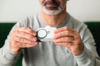 Homme qui tient à deux mains un petit détecteur blanc à installer au mur