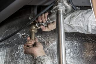 Mains qui serrent un raccord en laiton sur une canalisation sous un isolant aluminisé