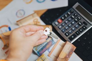 Main tenant une clé au-dessus de billets en euros et d'une calculatrice