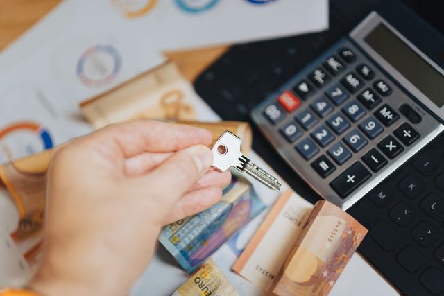 Remplacer sa chaudière avec MaPrimeRénov', les CEE, l'éco-PTZ et la TVA réduite Main tenant une clé au-dessus de billets en euros et d'une calculatrice