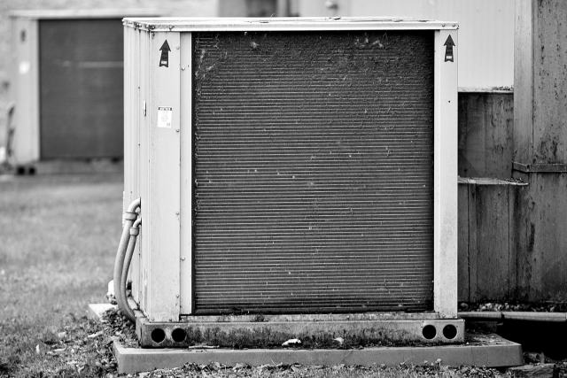 Choisir entre pompe à chaleur et chaudière selon votre logement Unité extérieure de pompe à chaleur posée sur un socle en béton, en noir et blanc