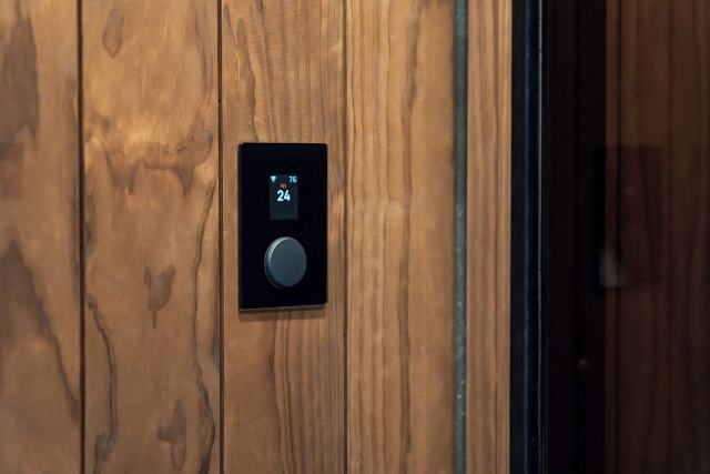Réguler sa chaudière avec un thermostat d'ambiance ou une sonde extérieure Thermostat d'ambiance noir à écran et molette encastré dans un lambris en bois
