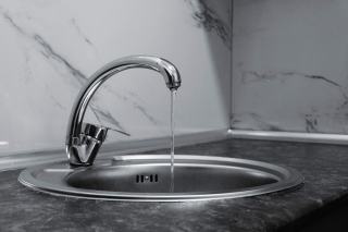Mitigeur chromé qui laisse couler un filet d'eau dans un évier rond en inox